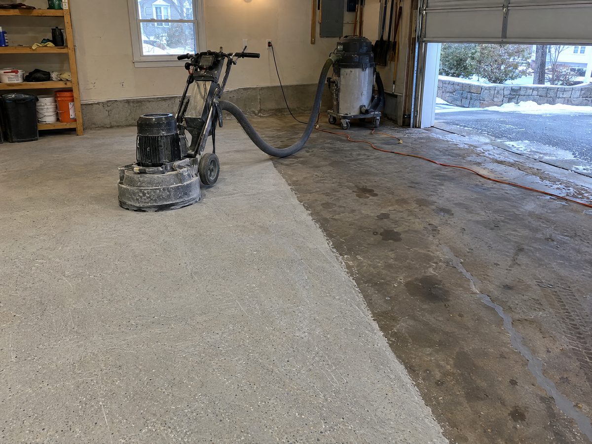 A garage slab half ground by a planetary grinder, the ground half light and even, the rest dark with oil stains and a filled crack